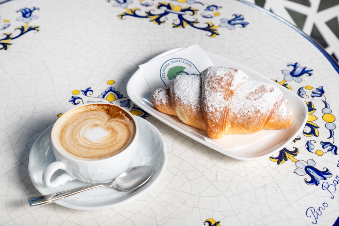 Colazione al Pino Bar Fano: cappuccino con latte art e cornetto al piatto di ceramica maiolicata